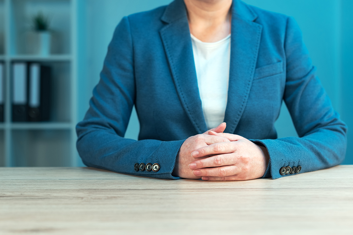Business negotiation skills with female executive sitting at office desk with confident pose and hands crossed, body language for determination and willpower