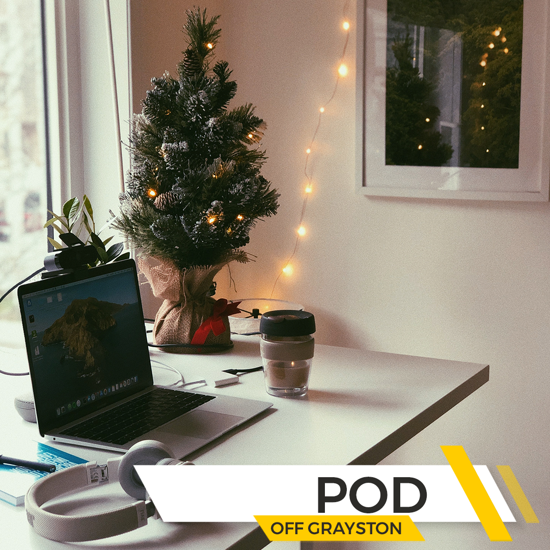 Cozy desk setup with a small decorated Christmas tree, laptop, and coffee cup in an office space, with branding for The POD Off Grayston.